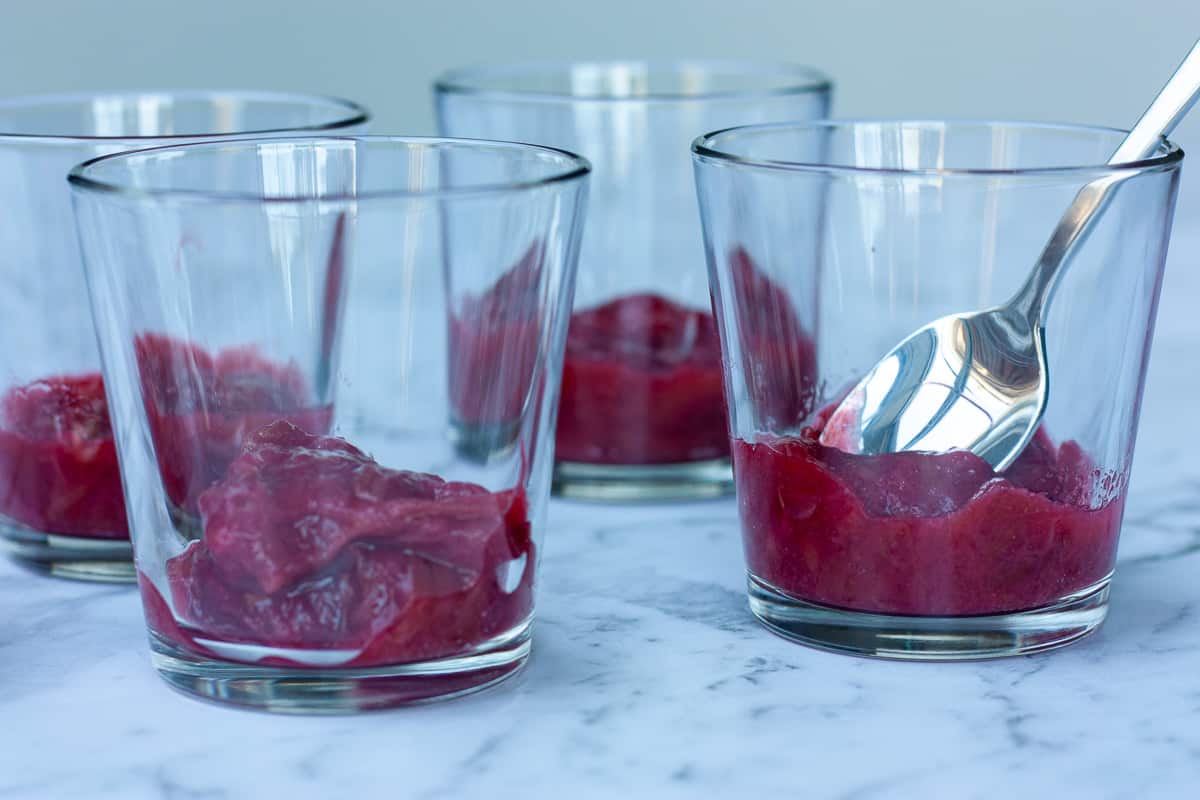 Side view of trifle glasses each containing a small mound of rhubarb compote.