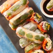 Plate of rice paper rolls, some cut in half to show rainbow-coloured fillings.