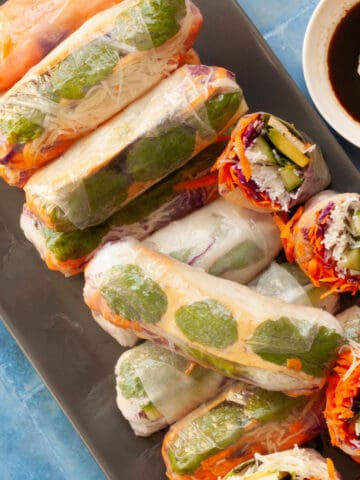 Plate of rice paper rolls, some cut in half to show rainbow-coloured fillings.