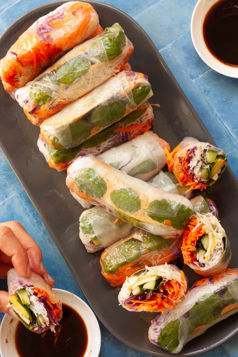 Plate of rice paper rolls, some cut in half to show rainbow-coloured fillings.