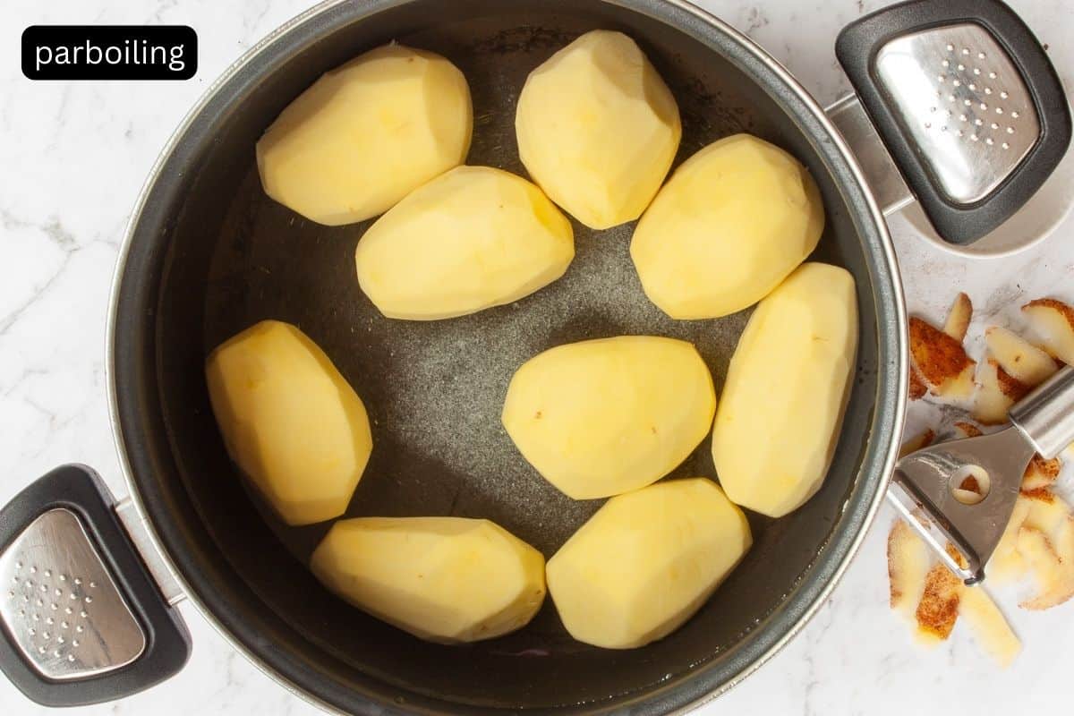 Whole peeled potatoes in a large saucepan containing salted water.