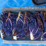 A row of roasted purple cabbage wedges overlapping on an oval grey plate.