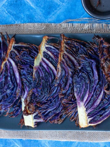 A row of roasted purple cabbage wedges overlapping on an oval grey plate.