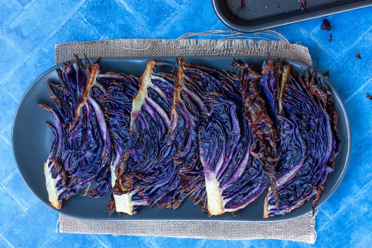 A row of roasted purple cabbage wedges overlapping on an oval grey plate.