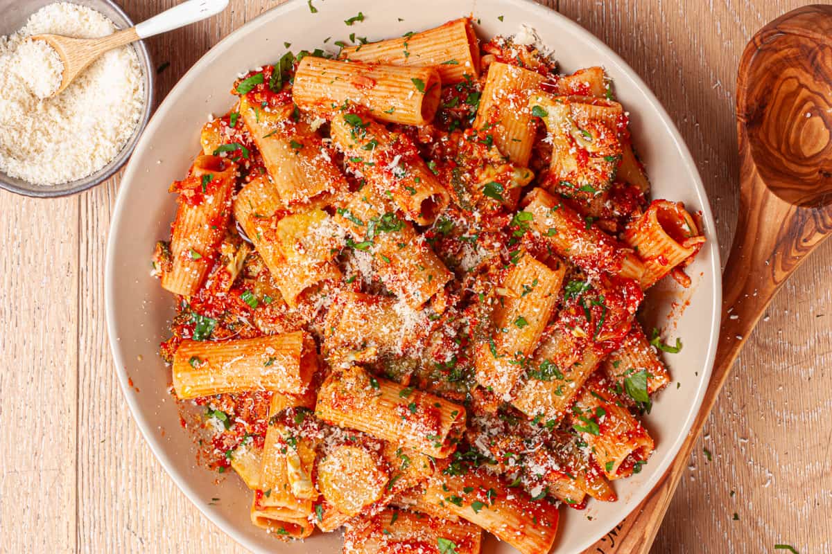 Large white plate filled with rigatoni in a tomato sauce, dusted with grated cheese and parsley flecks.