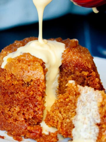 Custard being poured over a whole steamed pudding.