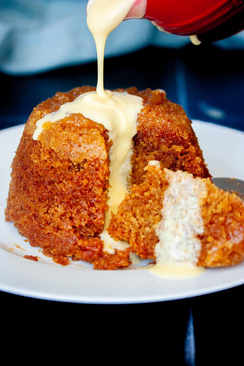 Custard being poured over a whole steamed pudding.