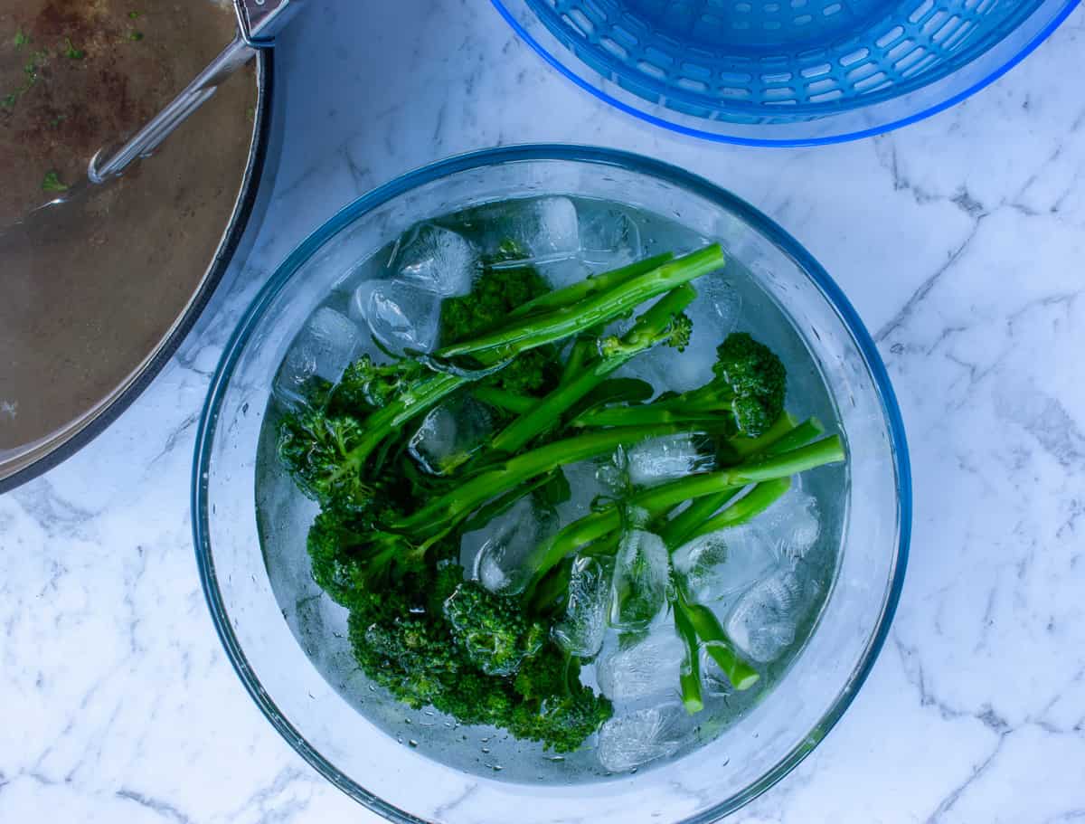 Bright green broccolini stems in a bowl of iced water.