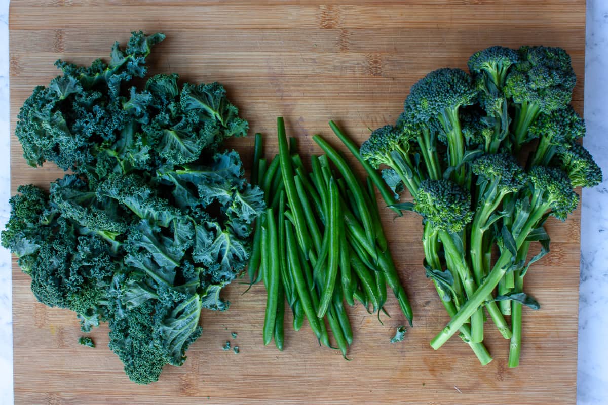 Prepped green veg laid out on a wooden chopping board.