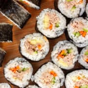 Bitesize rounds of sushi on a wooden board - some on their sides.