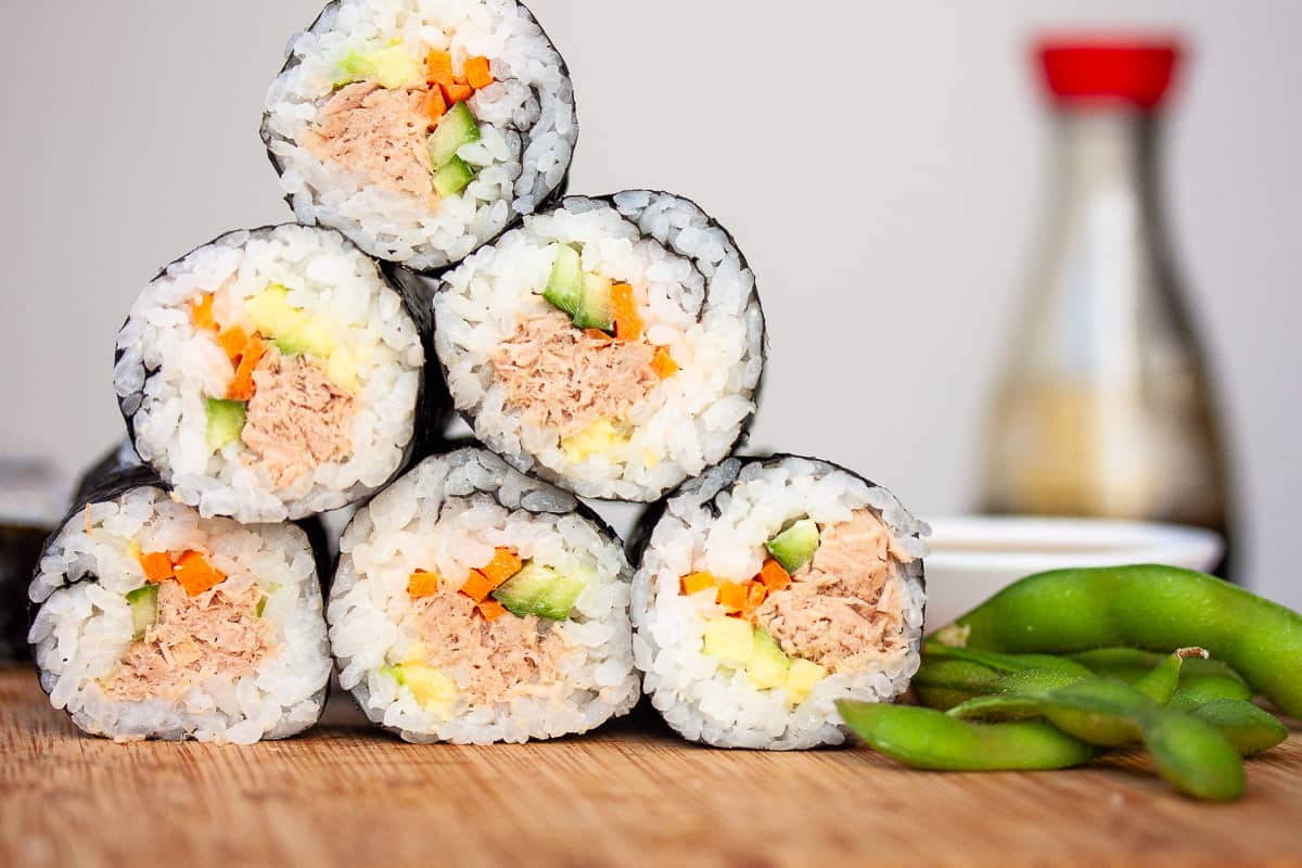 A stack of hand rolls arranged in a pyramid. Some edamame beans to the side.