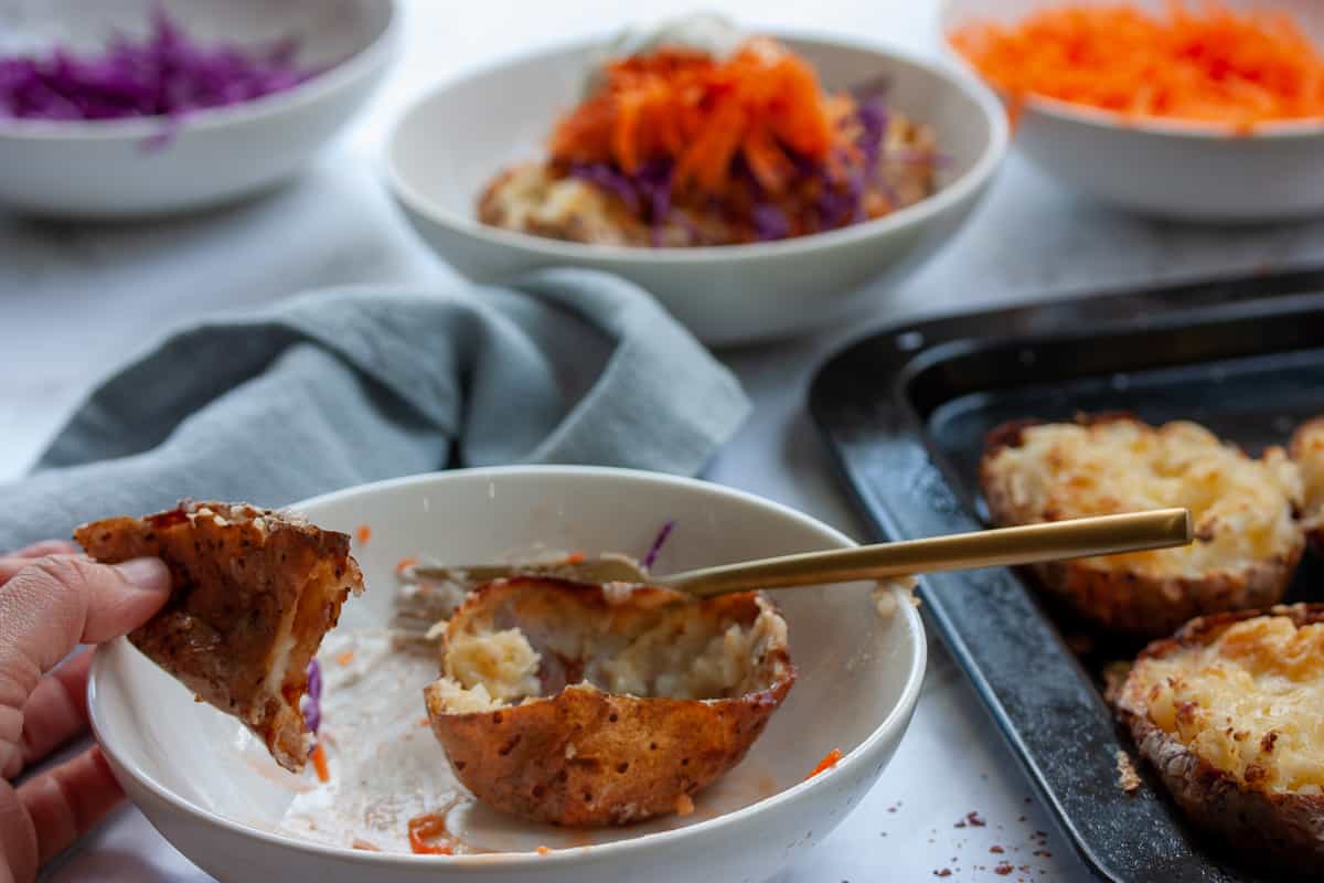 Empty crispy potato skin half in a bowl. The other half is held in a hand with a bite taken out of it.