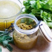 Glass jar containing vegetable stock paste. A glass measuring jug with made up stock in the background.