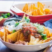 Bowl of cheesy nachos loaded with guacamole, salsa and soured cream.