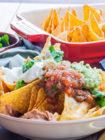 Bowl of cheesy nachos loaded with guacamole, salsa and soured cream.