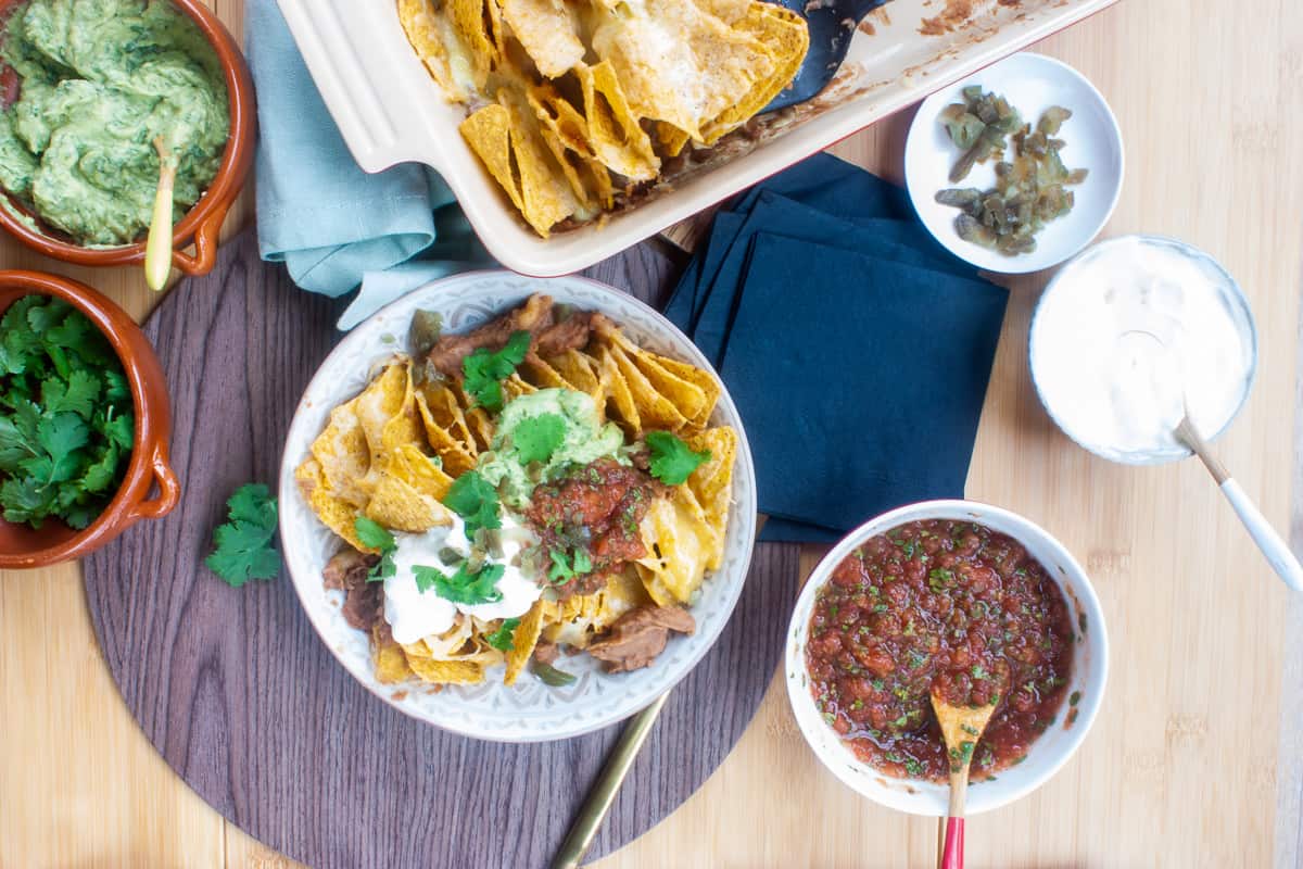 A bowl of loaded nachos surrounded by smaller bowls of toppings.